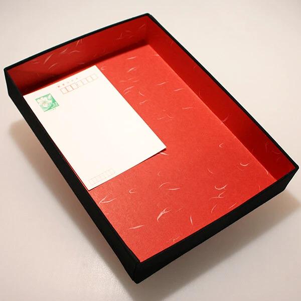 a red and black box with a white paper card inside it, placed on a white surface.