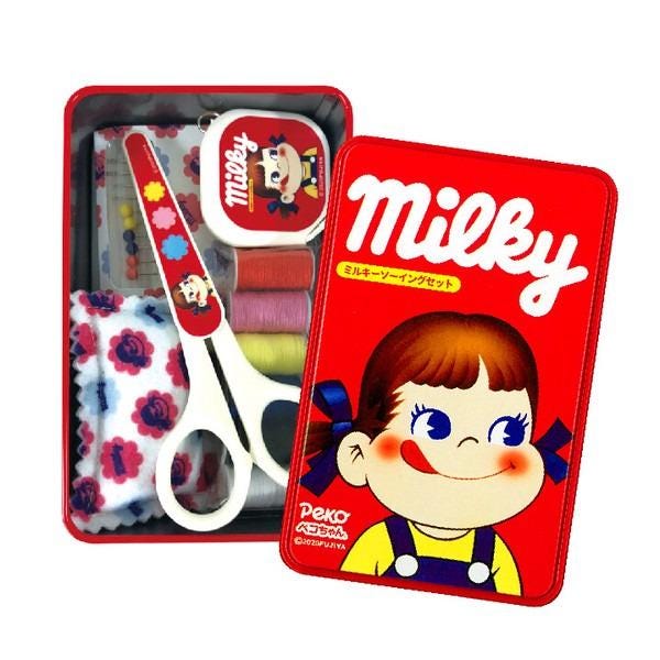 A red tin box containing various sewing and crafting supplies, including a pair of scissors, a sewing kit, and a character design.