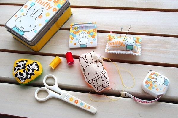 A collection of craft supplies, including a pair of scissors, a sewing kit, and various decorative items, arranged on a wooden surface.