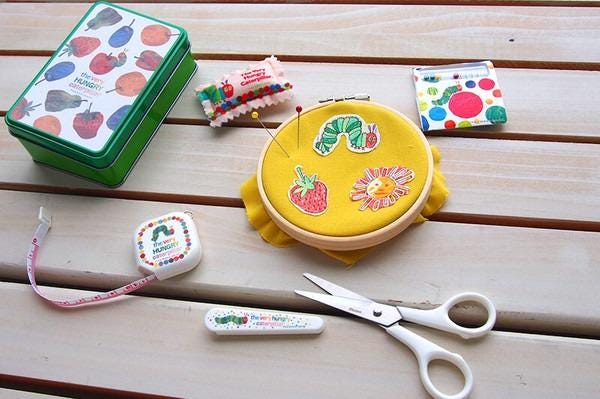 A collection of craft supplies, including a yellow embroidery hoop, scissors, and other colorful items, arranged on a wooden surface.