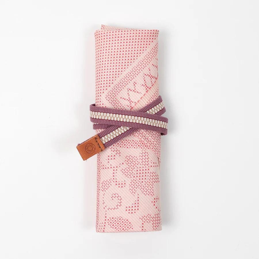 A pink and white patterned cloth rolled up and tied with a purple and white striped ribbon.