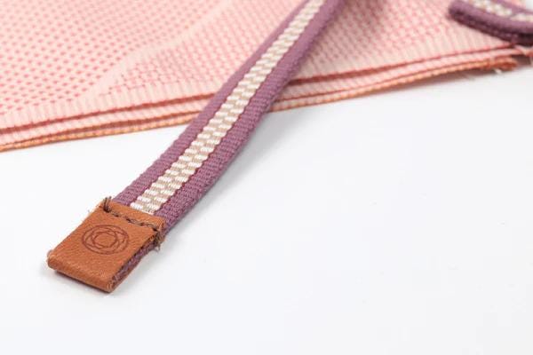 A close-up view of a purple and white striped fabric item, possibly a piece of clothing or accessory, with a brown leather clasp or fastening attached.
