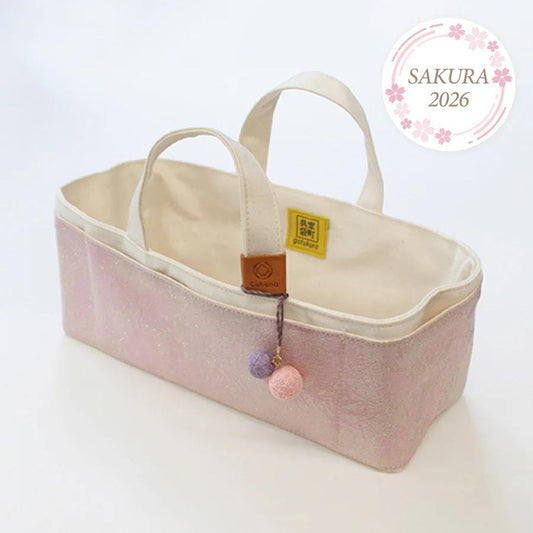 A pink and white tote bag with a small yellow tag and a pink and purple ball attached, placed on a white surface.