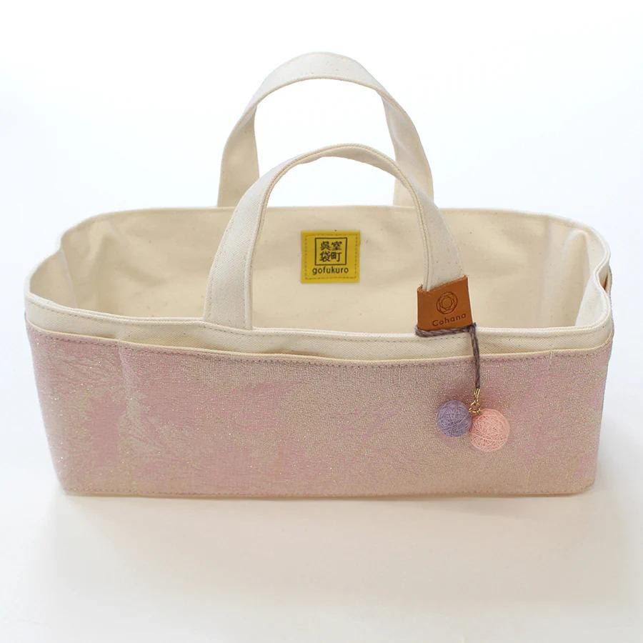 A pink and white tote bag with a small charm hanging from the handle.