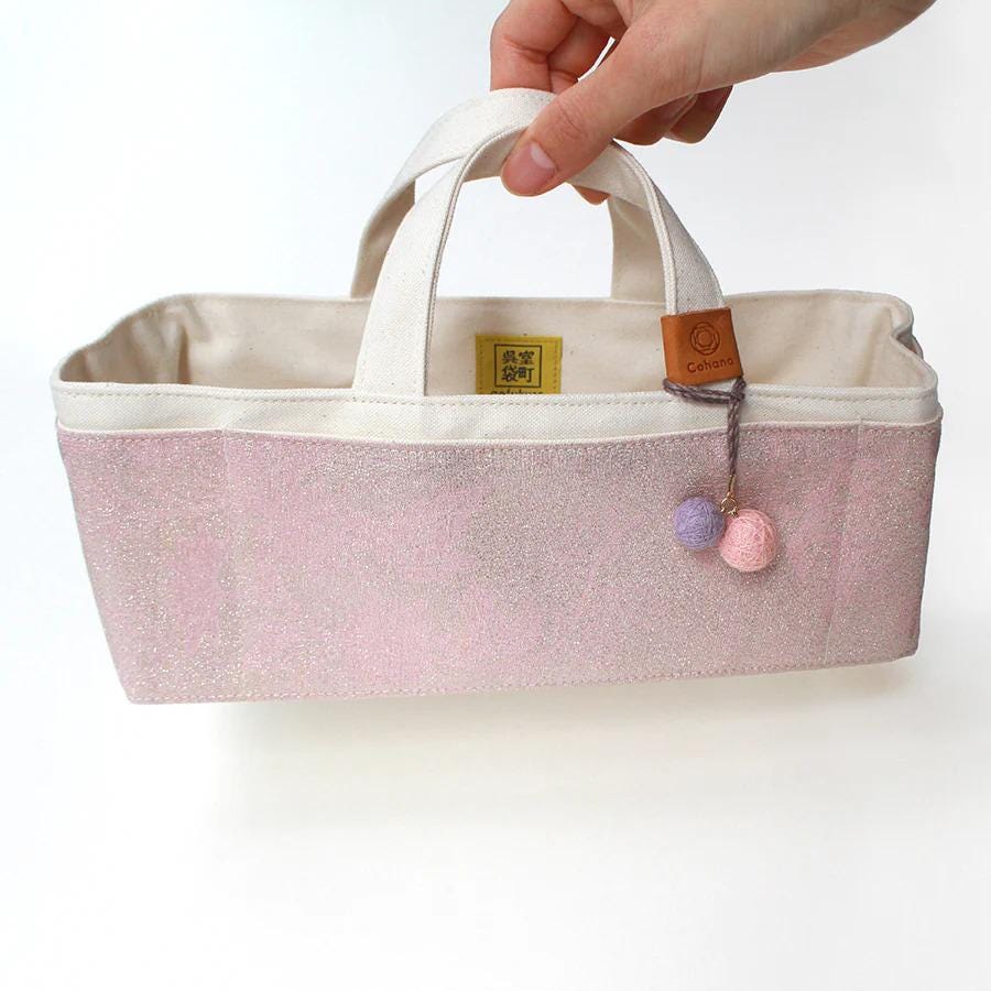 A hand holding a pink and white tote bag with a small tag attached.