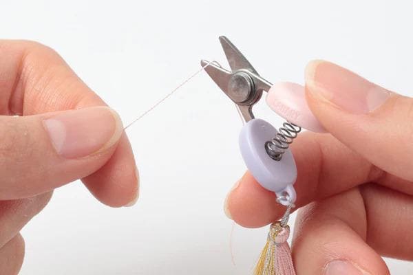 A pair of hands holding a pair of scissors and cutting a string.