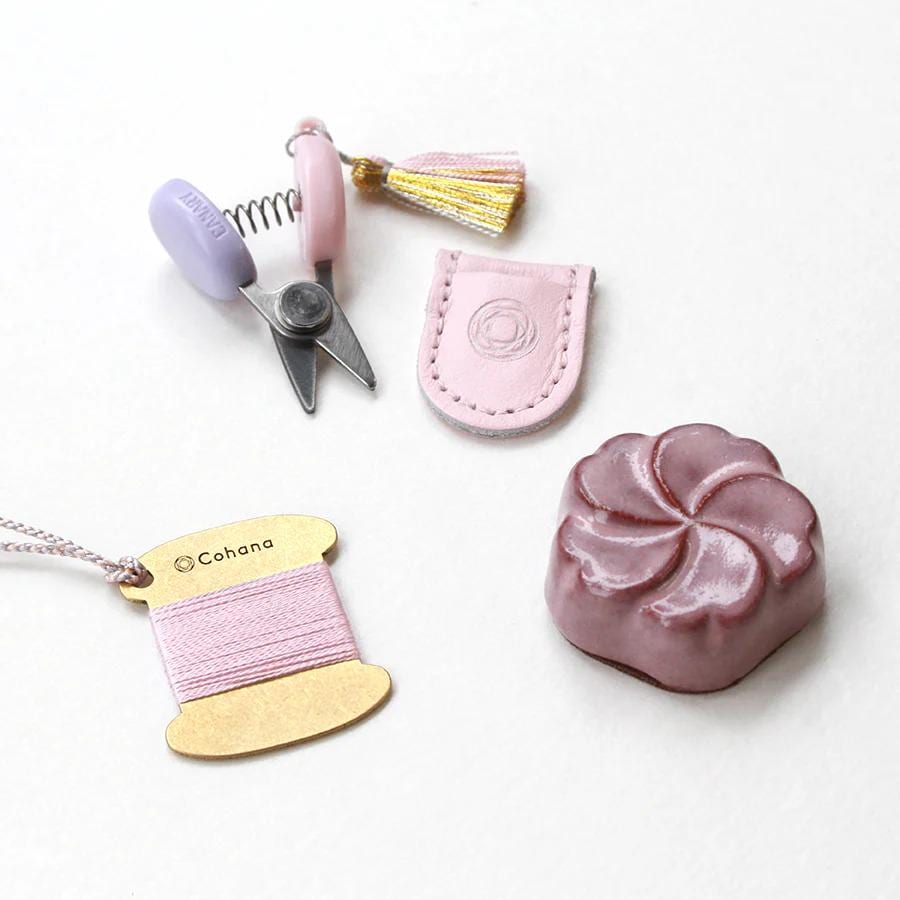 various craft supplies, including a pair of scissors, a tassel, a leather pouch, a spool of thread, and a small pink object resembling a flower.