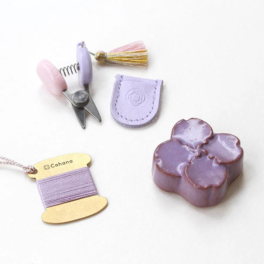 a collection of craft supplies, including a pair of scissors, a leather pouch, a tassel, and a purple flower-shaped object.