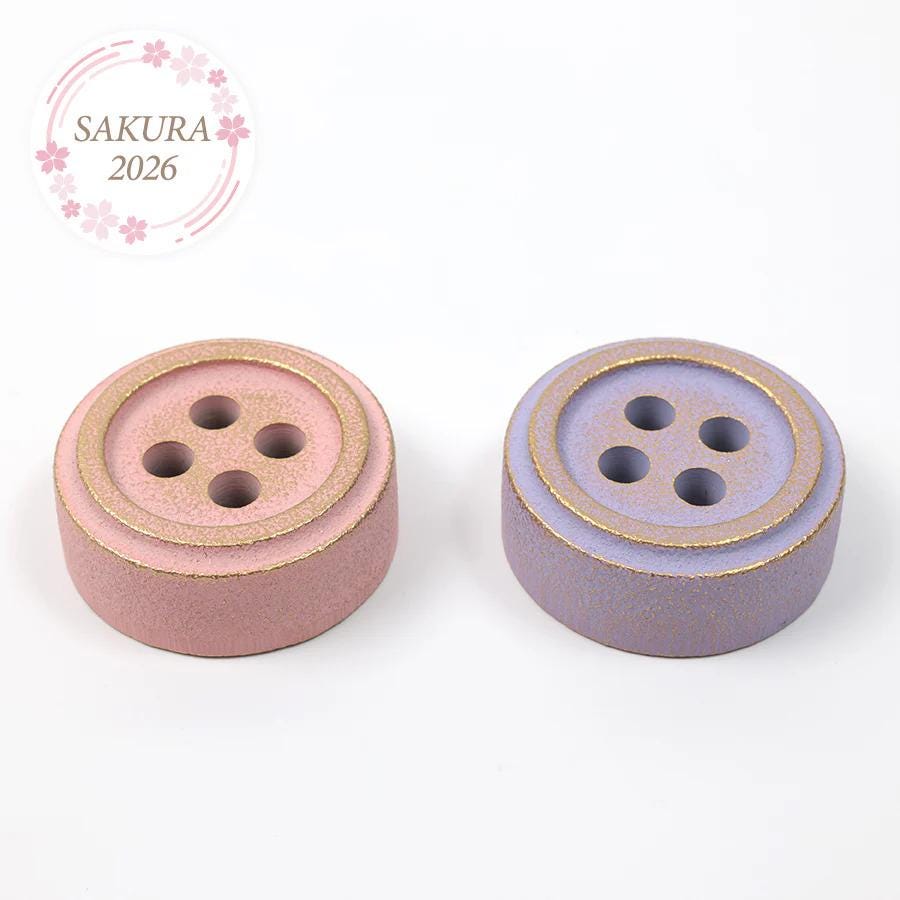 two round, metallic buttons with gold and purple coatings, placed side by side on a white background.