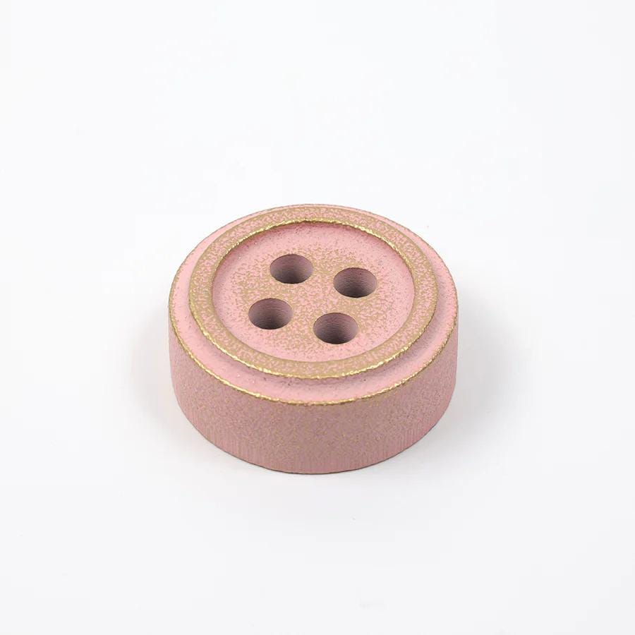 A pink button with gold trim is shown against a white background.