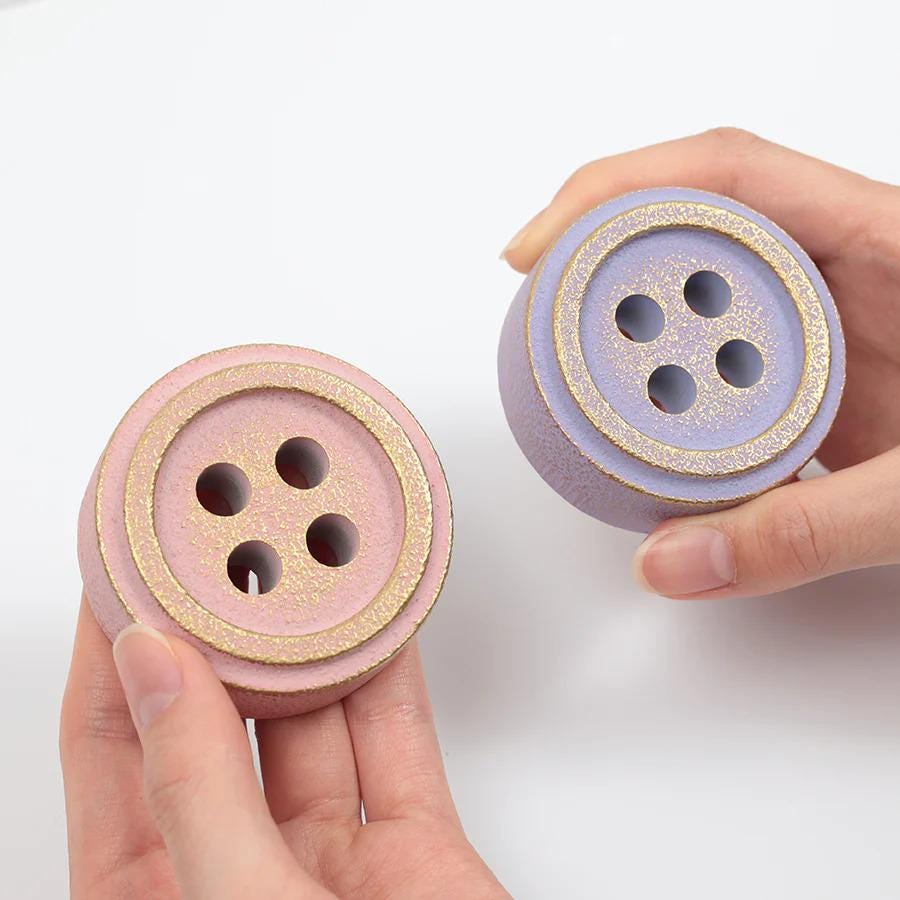 A pair of hands holding two small, round objects with gold and purple colors.
