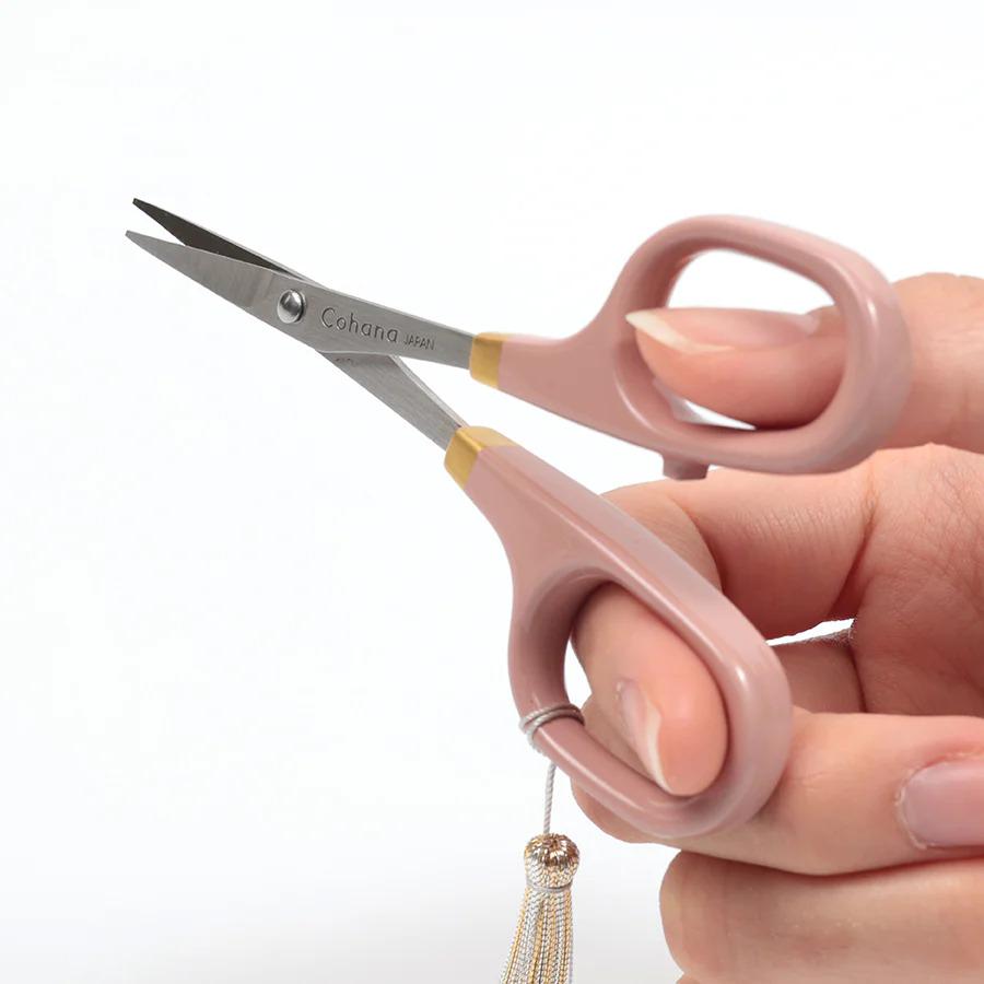 A hand holding pink-handled scissors with a tassel hanging from the handle.