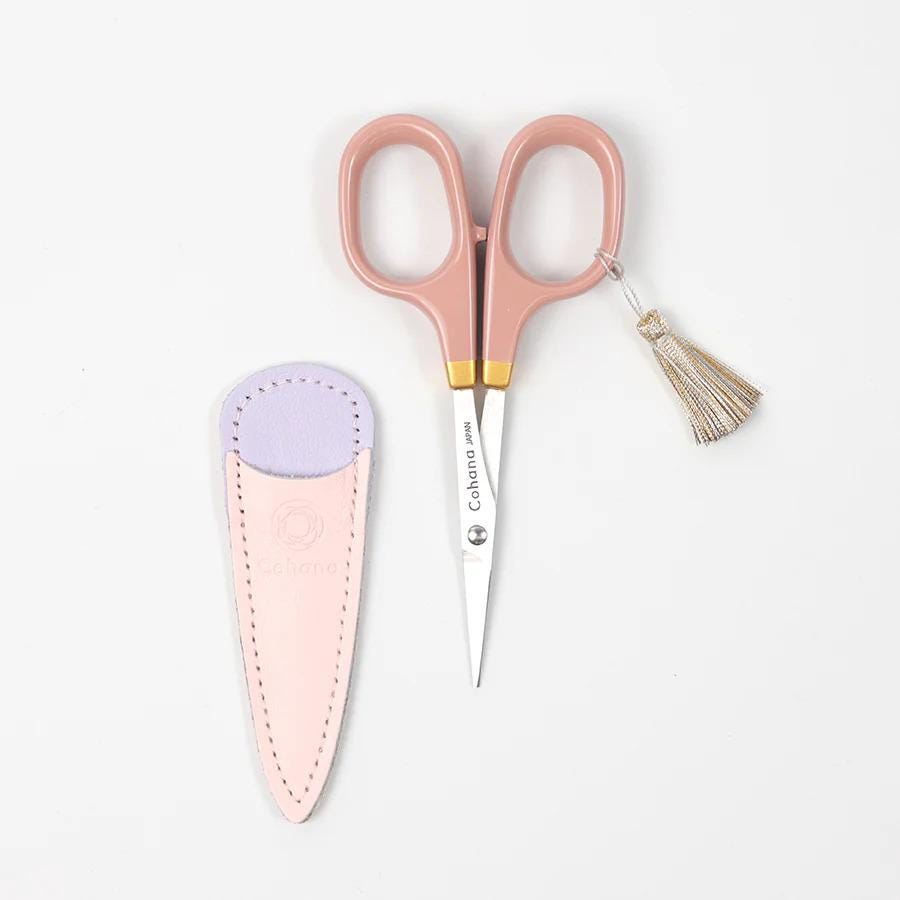 A pair of pink scissors and a pink and purple leather scissor holder are placed on a white background.