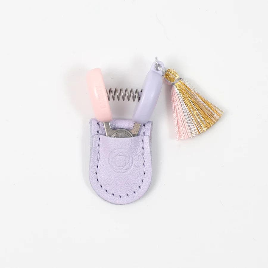 A pair of scissors with a purple handle and a pink spring mechanism, placed in a small purple leather pouch with a tassel.