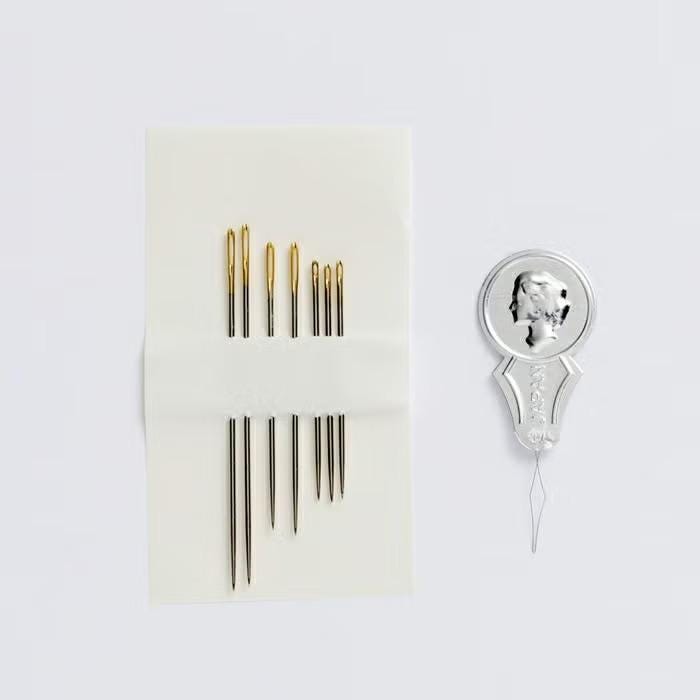 a collection of sewing needles and a silver pin holder on a white background.