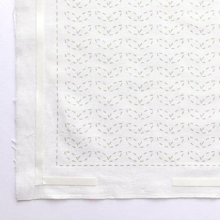 a close-up view of a white fabric with a repeating pattern of green leaves or flowers. The pattern is visible on the fabric, creating a visually appealing design.