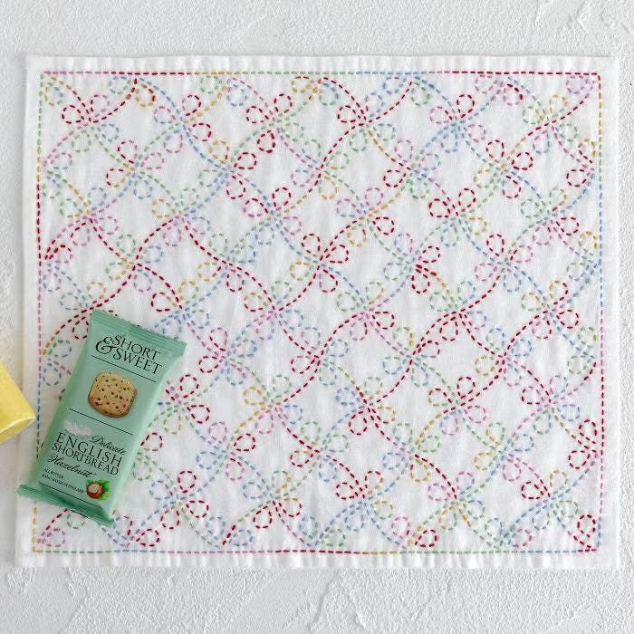a small square with a colorful, hand-stitched floral pattern on it, along with a small package of cookies placed next to it.