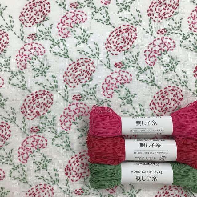 three spools of thread with a floral pattern on them, placed on a white fabric with a similar floral pattern.