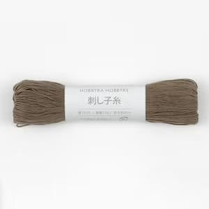 A spool of brown yarn with a label that reads "HOBBRA HOBBRÄTRE" and "素足素足" (which means "light brown" in English).