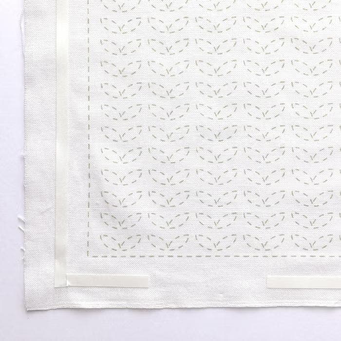 a close-up view of a white fabric with a repeating pattern of green leaves or flowers. The pattern is visible on the fabric, creating a visually appealing design.