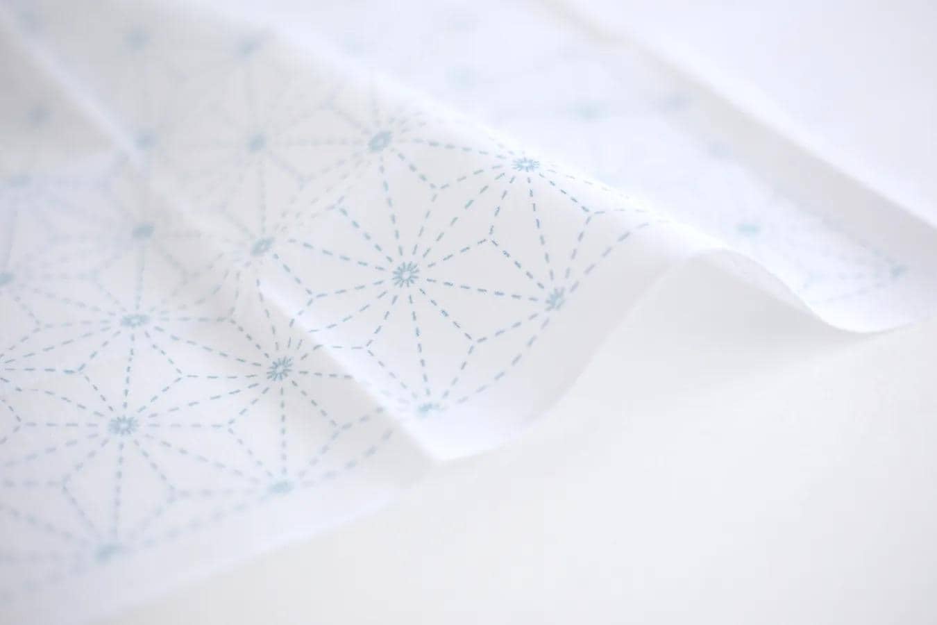 a close-up view of a white fabric with a blue geometric pattern, featuring a repeating star-like design.