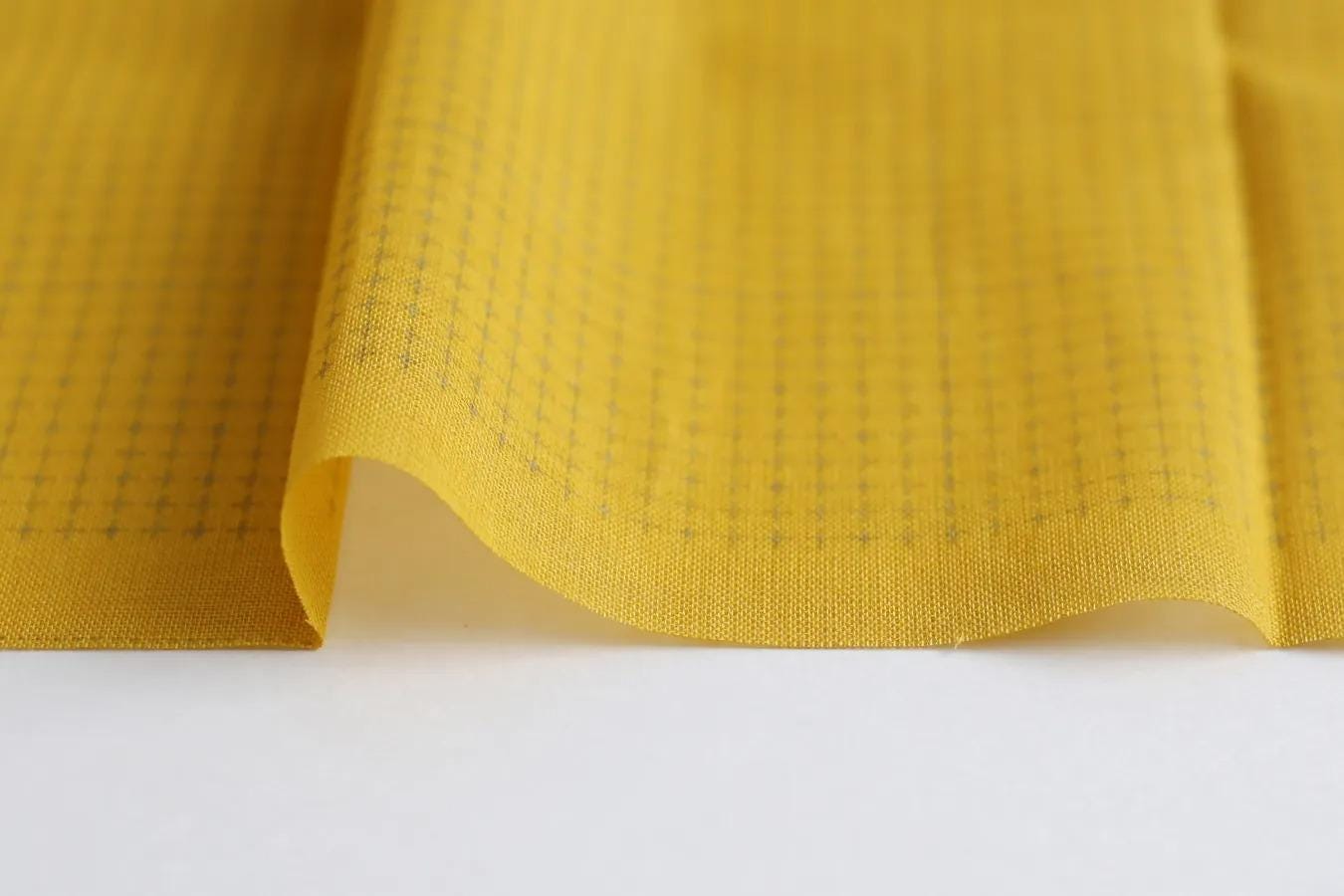 A close-up view of a yellow fabric with a grid pattern, folded over itself to create a wave-like shape.