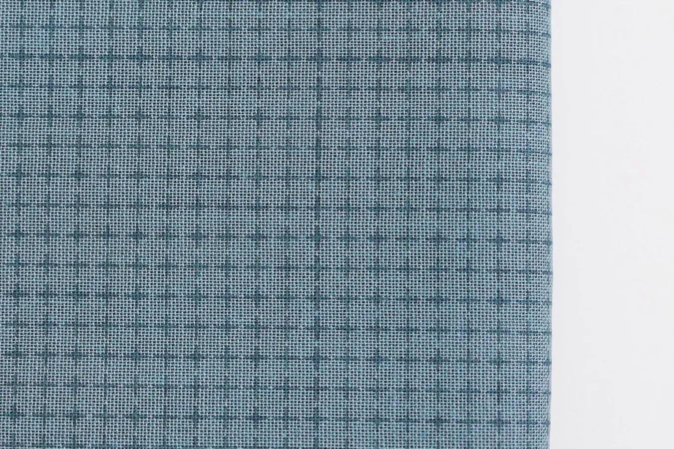 a close-up view of a fabric with a grid-like pattern of small squares or rectangles in shades of blue and gray.