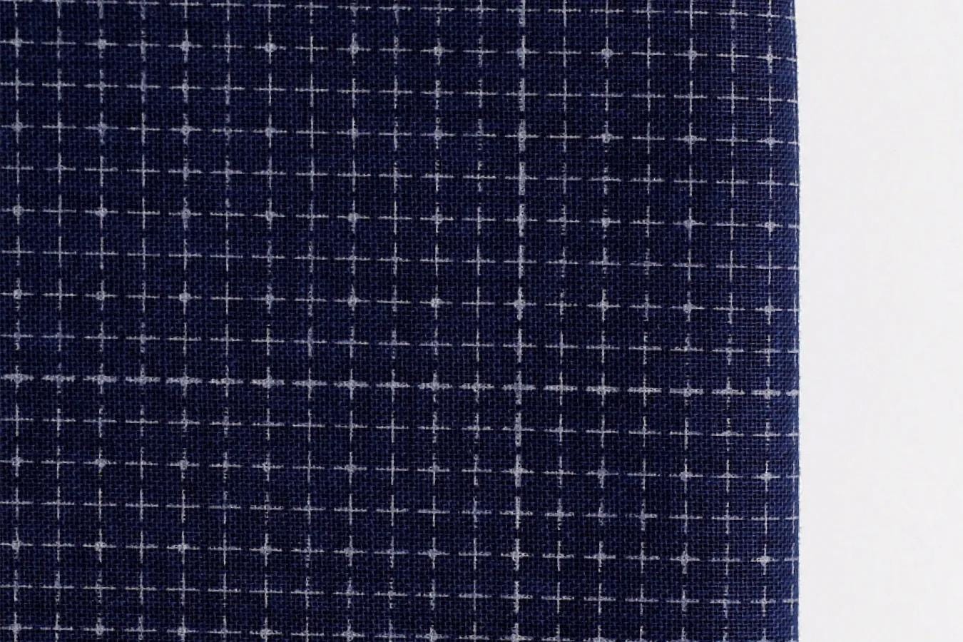 a close-up view of a dark blue fabric with a grid-like pattern of white crosses or dots.
