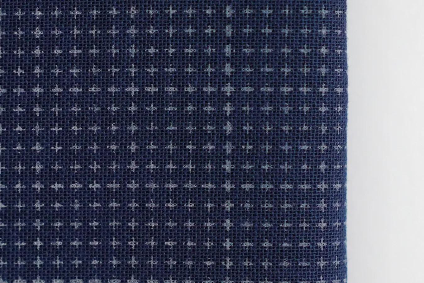 a close-up view of a dark blue fabric with a white pattern, featuring a grid-like design.