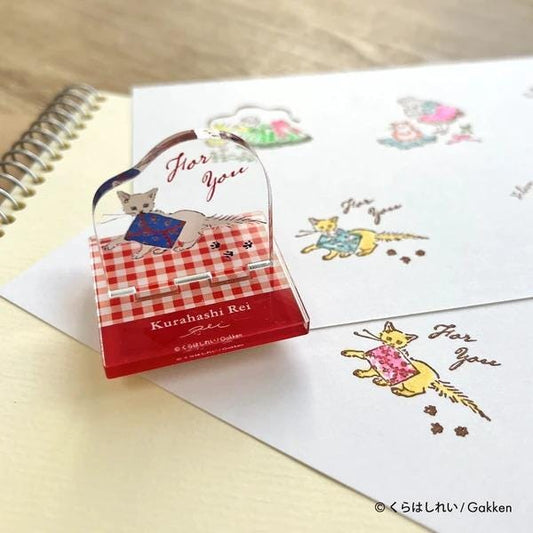 a red and white paper with a cat illustration and the text "For You" written on it. There is also a small red and white paperweight with a cat illustration on it, placed on top of the larger paper.