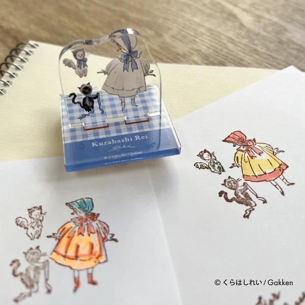 A clear stamp featuring illustrations of a girl and a cat, along with a blue and white checkered background. The stamp is placed on top of a piece of paper with hand-drawn illustrations of a girl and a cat.