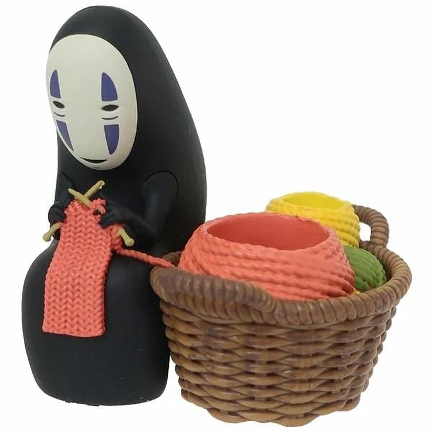 A figurine of a character with a black face and a knitted scarf is sitting next to a basket filled with various objects, including balls and a red bowl.
