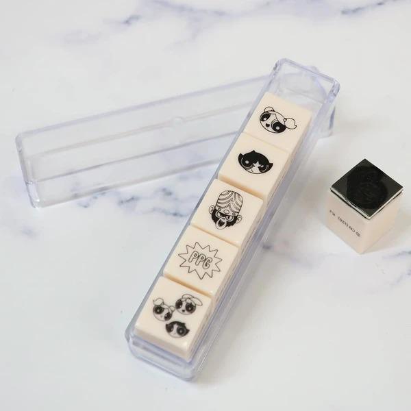 A clear plastic container with five small, cartoon-style stamps on it, along with a small square object next to the container.
