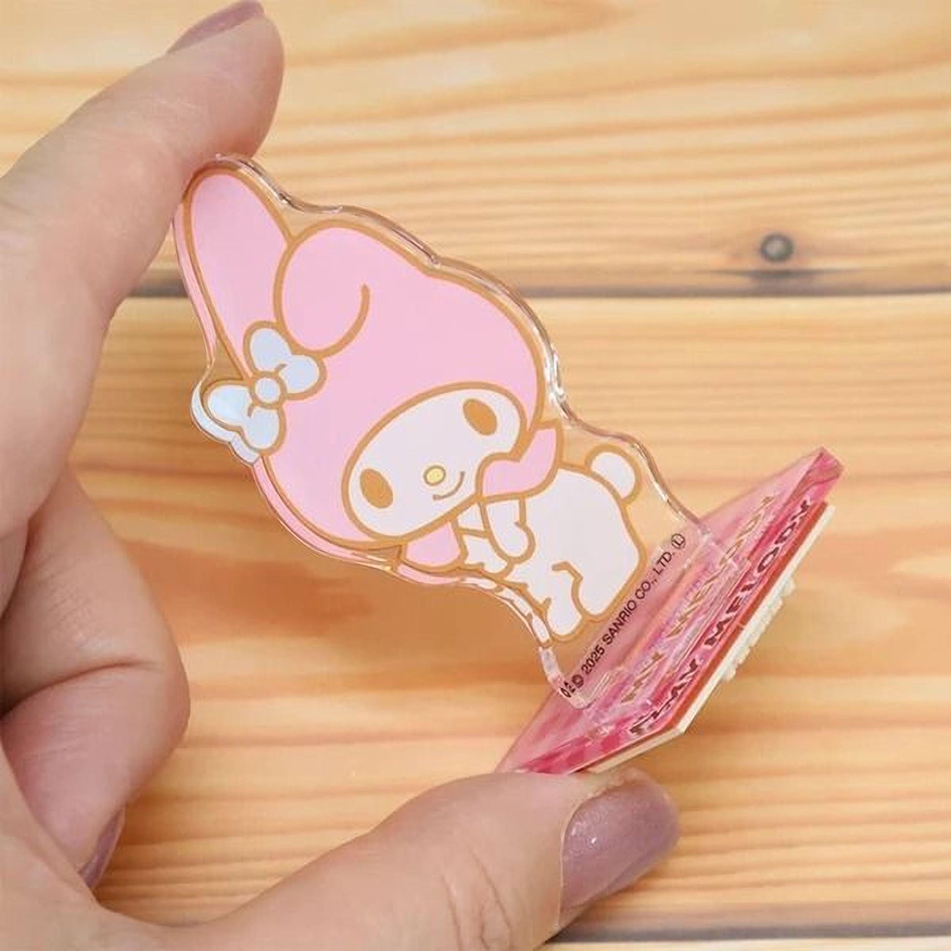 A hand is holding a clear plastic object with a pink and white cartoon character design on it.