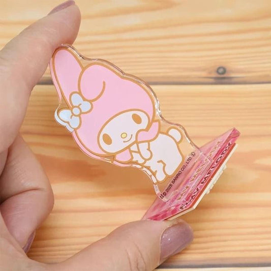 A hand is holding a clear plastic object with a pink and white cartoon character design on it.
