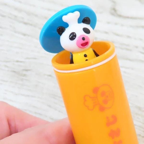 A small toy panda wearing a chef's hat is sitting inside an orange tube with a red and white design.