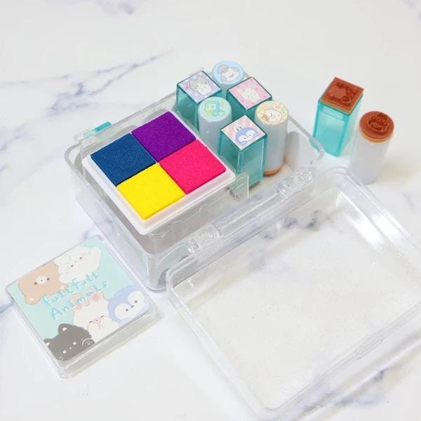 A clear plastic container filled with colorful foam stamps and a small clear plastic container with a lid, both placed on a marble surface.