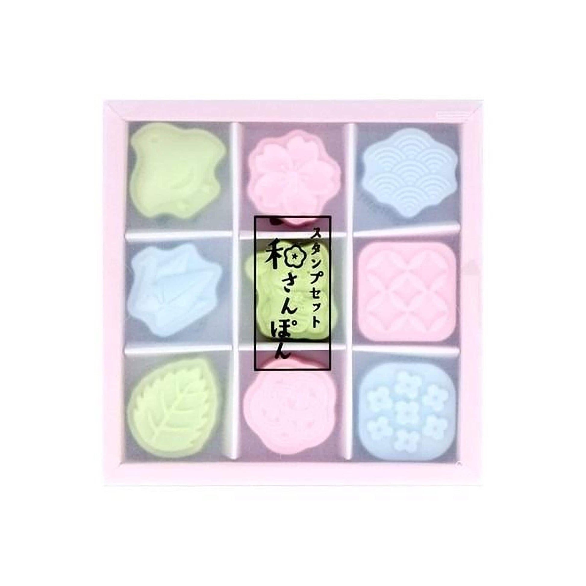 A pink box containing nine colorful, pastel-colored shapes, including a flower-shaped object, a leaf-shaped object, and other abstract shapes.