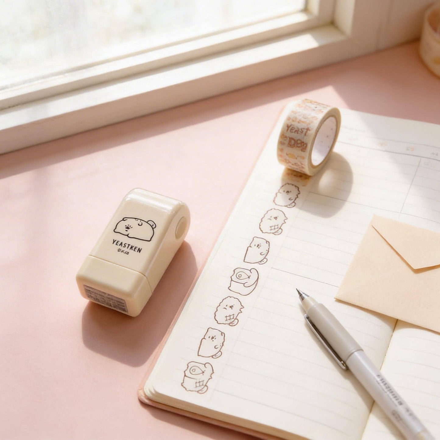 a pink notebook with a pen, a roll of tape, and a stamp on a desk.