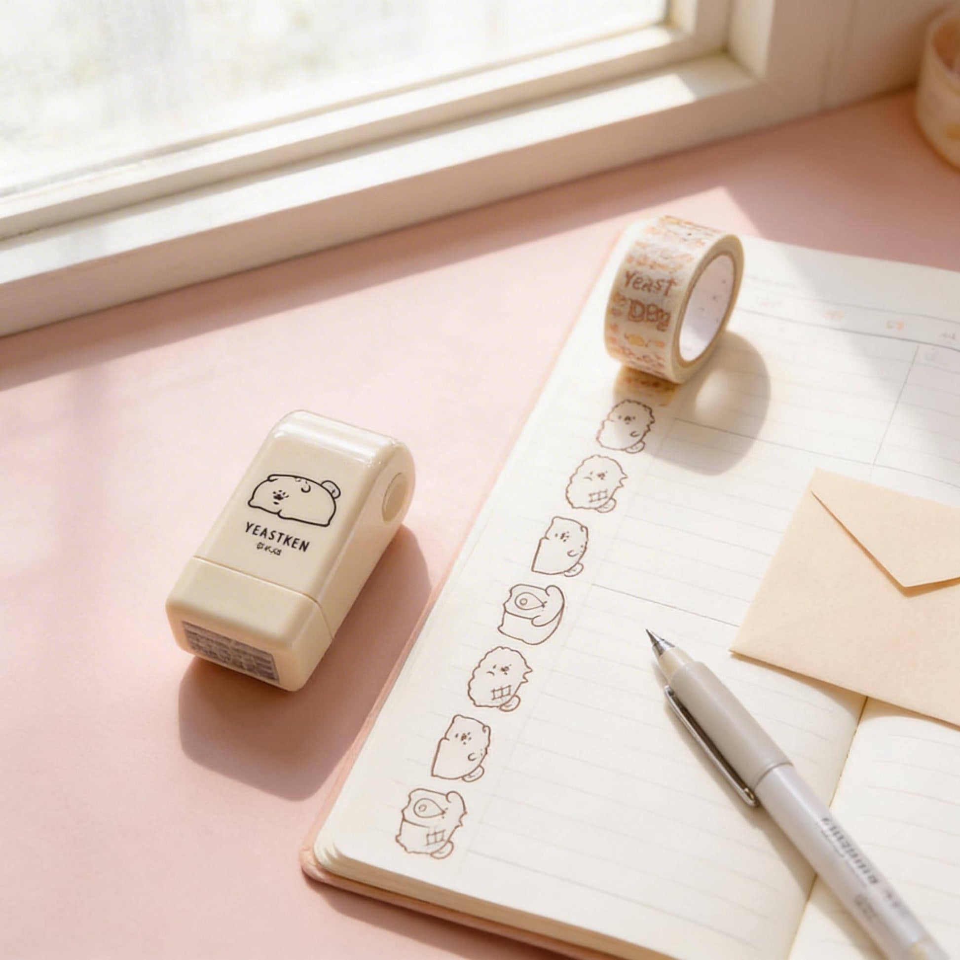 a pink notebook with a pen, a roll of tape, and a stamp on a desk.