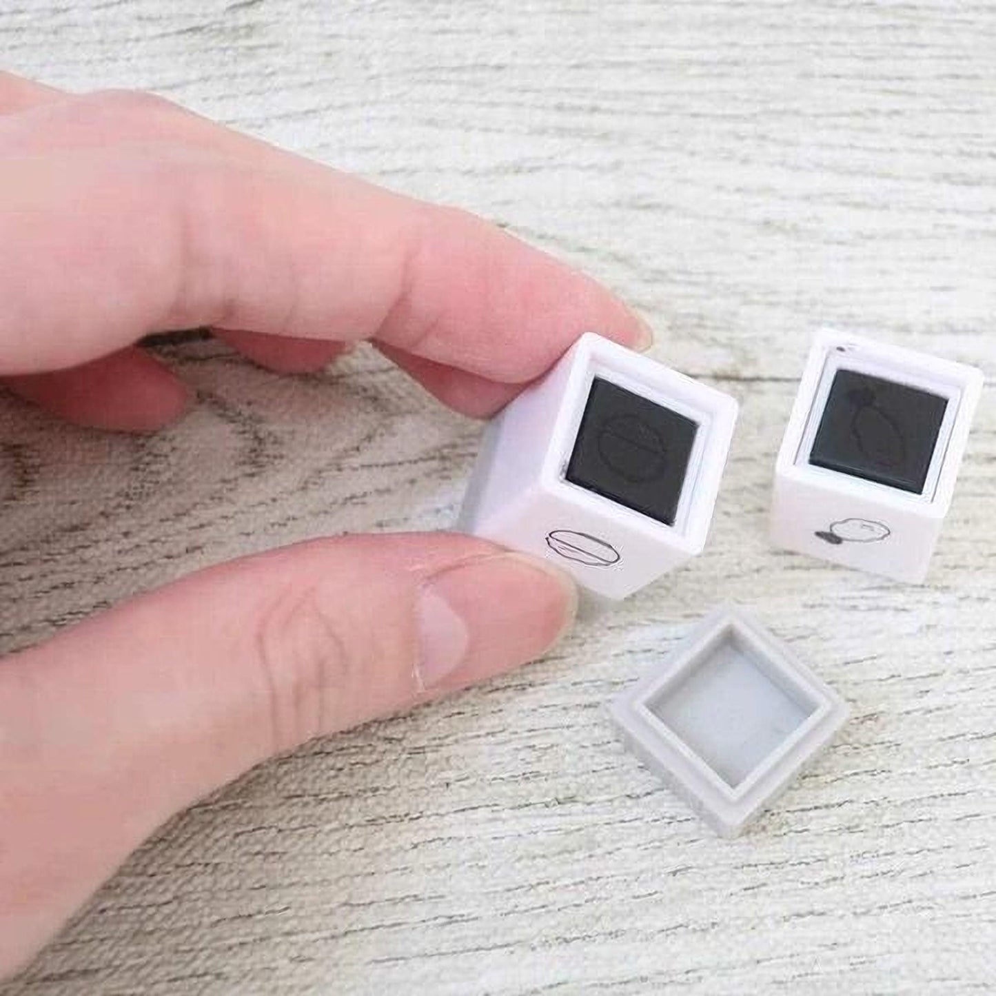 A person's hand is holding two small white cubes with black markings on a wooden surface.