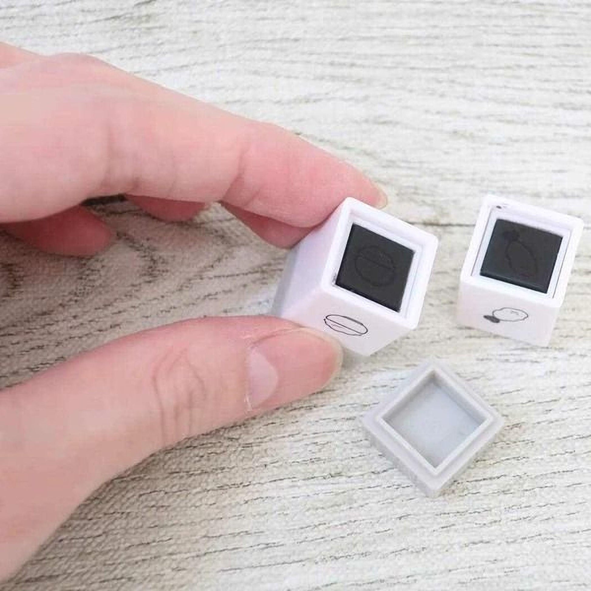 A person's hand is holding two small white cubes with black markings on a wooden surface.