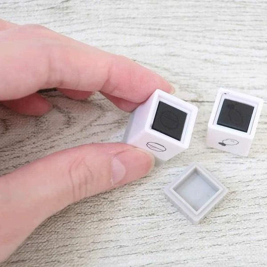 A person's hand is holding two small white cubes with black markings on a wooden surface.