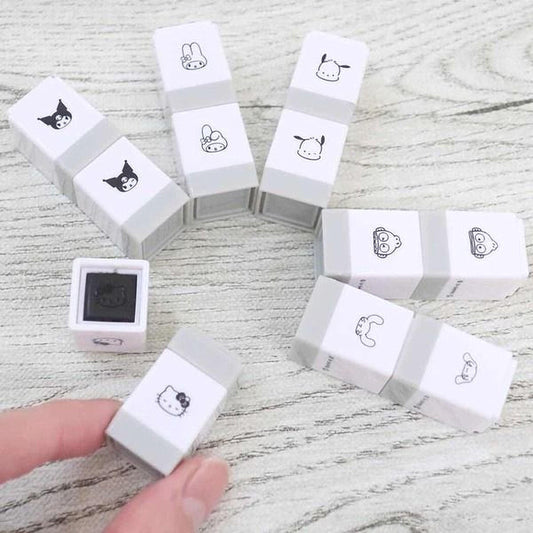 A collection of gray and white eraser stamps featuring various cartoon animal faces, including a Hello Kitty stamp, arranged on a wooden surface.