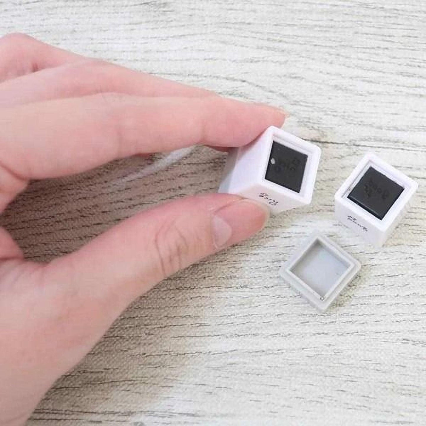A hand is holding two small white square objects with black markings on a wooden surface.