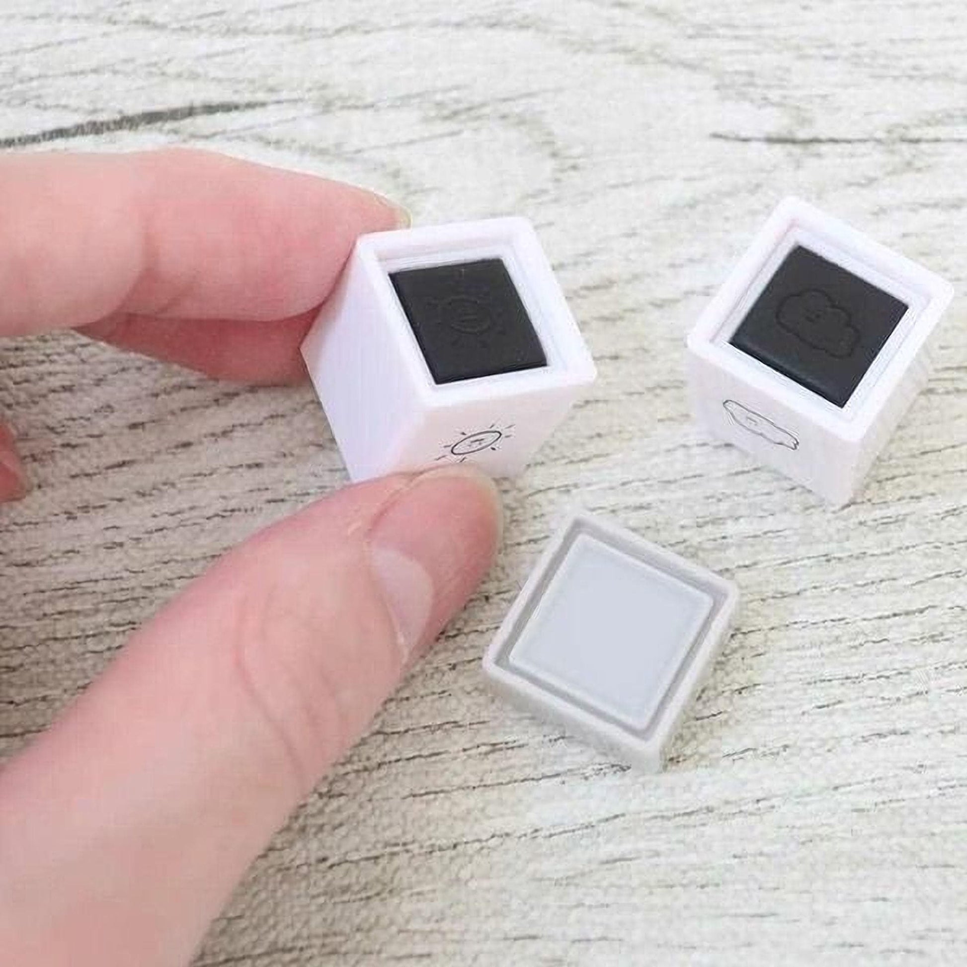 A person's hand is holding two small white cubes with black symbols on them, which appear to be weather-related icons.