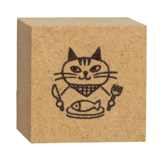 A square block with a black and white drawing of a cat holding a fish and a spoon.