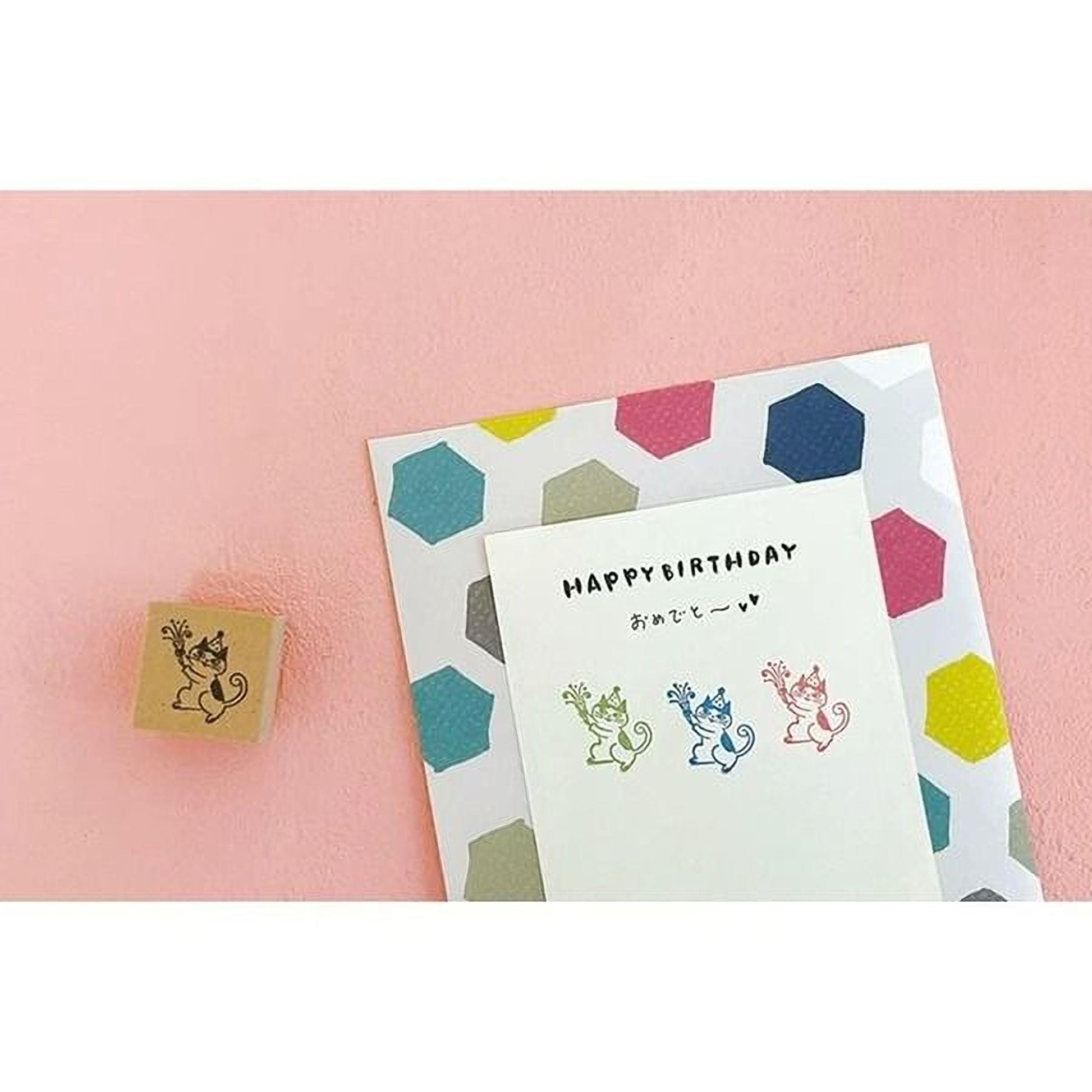 a birthday card with a colorful hexagonal pattern and a stamp of a cartoon character on a pink background.