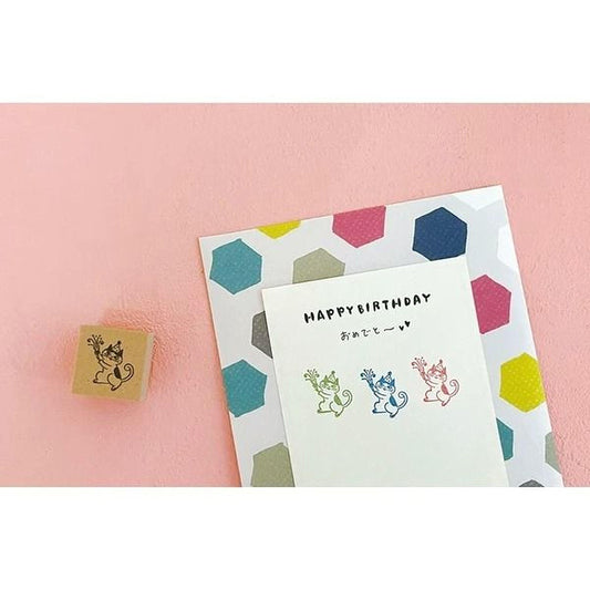 a birthday card with a colorful hexagonal pattern and a stamp of a cartoon character on a pink background.