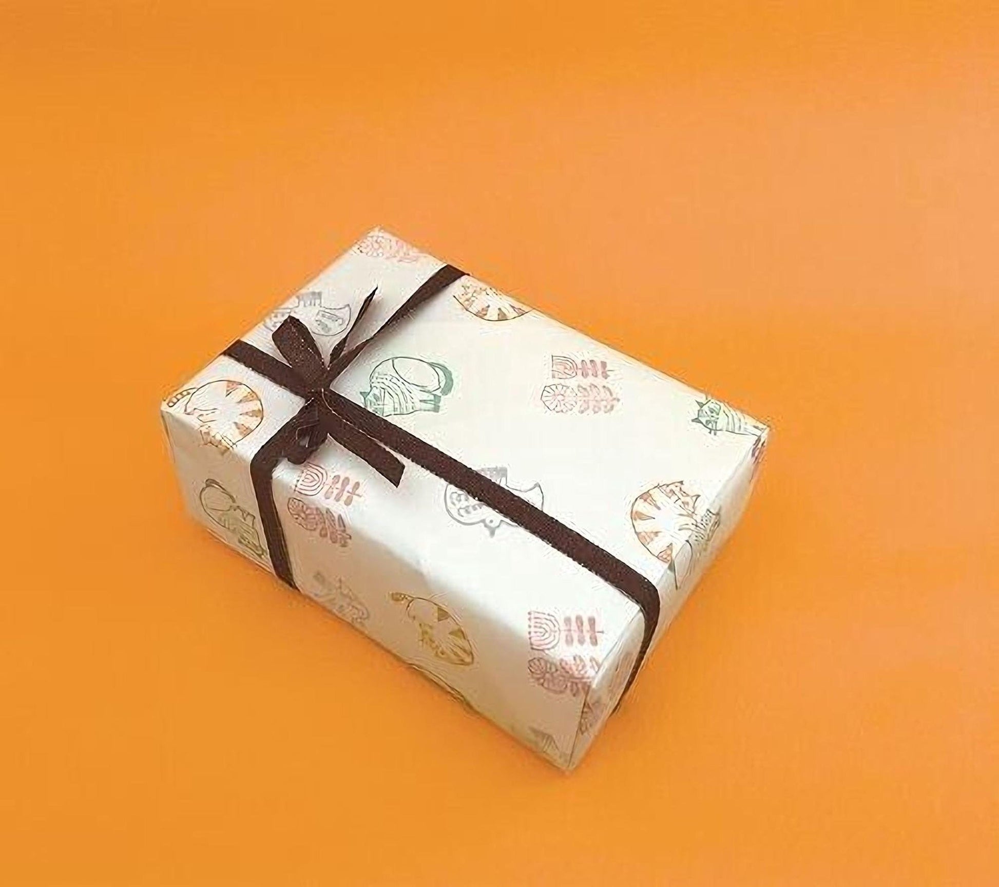 A gift box with a brown ribbon tied around it, featuring a repeating pattern of cat illustrations on a white background.